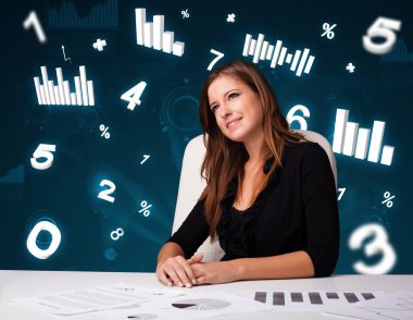 Masasında şema ve istatistiklerle oturan genç iş kadını.