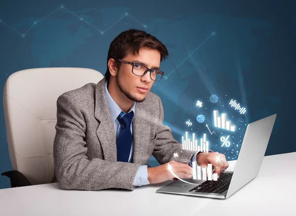 Young man sitting at desk and typing on laptop with diagrams and — Stock Photo, Image