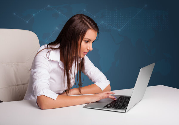 Молодая женщина сидит за столом и печатает на ноутбуке