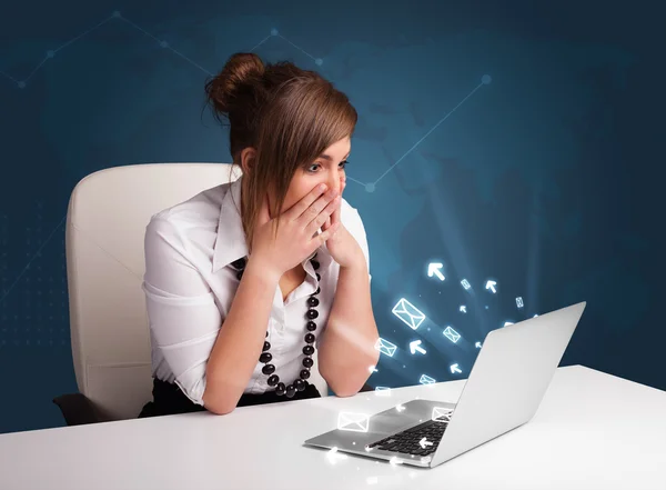 Young lady sitting at dest and typing on laptop with message ico — Stock Photo, Image