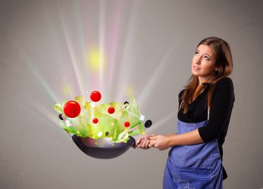 Genç bir kadın taze sebze pişiriyor.