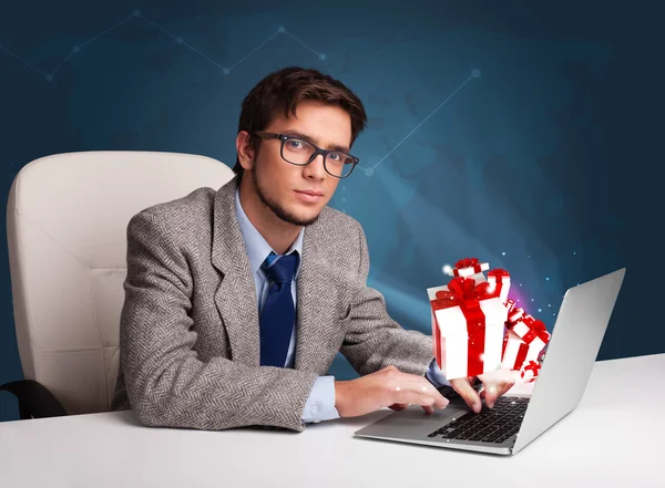 Hombre guapo sentado en el escritorio y escribiendo en el ordenador portátil con presente b —  Fotos de Stock