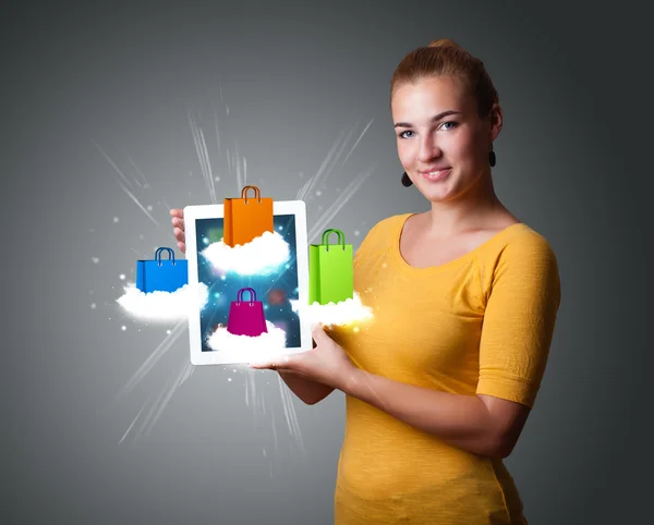 Mulher segurando tablet moderno com sacos de compras coloridos na nuvem — Fotografia de Stock