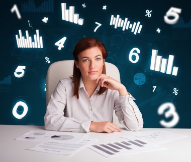 Masasında şema ve istatistiklerle oturan genç iş kadını.
