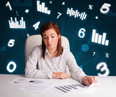 Masasında şema ve istatistiklerle oturan genç iş kadını.