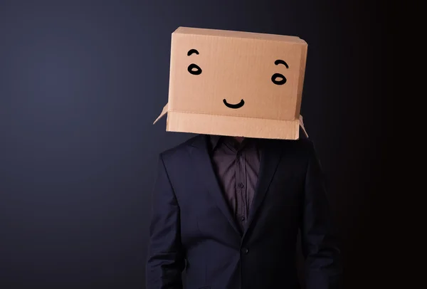 Young man gesturing with a cardboard box on his head with smiley — Stock Photo, Image