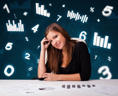 Masasında şema ve istatistiklerle oturan genç iş kadını.