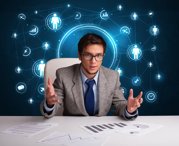 Businessman sitting at desk with social network icons — Stock Photo, Image