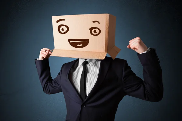 Forretningsmand gestikulerer med en papkasse på hovedet med smil - Stock-foto