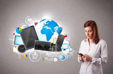 Genç bir kadın ayakta ve telefonunda geziniyor.