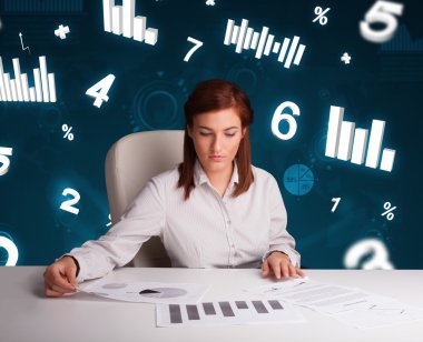 Masasında şema ve istatistiklerle oturan genç iş kadını.