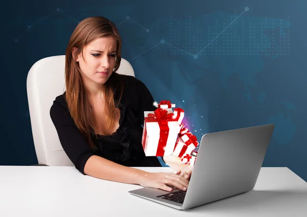 Pretty lady sitting at desk and typing on laptop with present bo — Stock Photo, Image