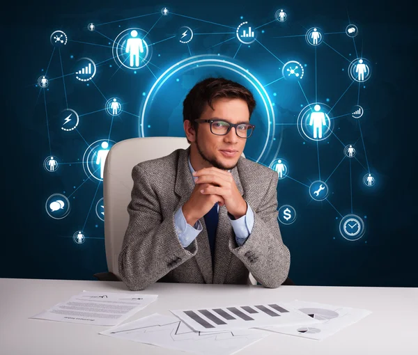 Businessman sitting at desk with social network icons — Stock Photo, Image