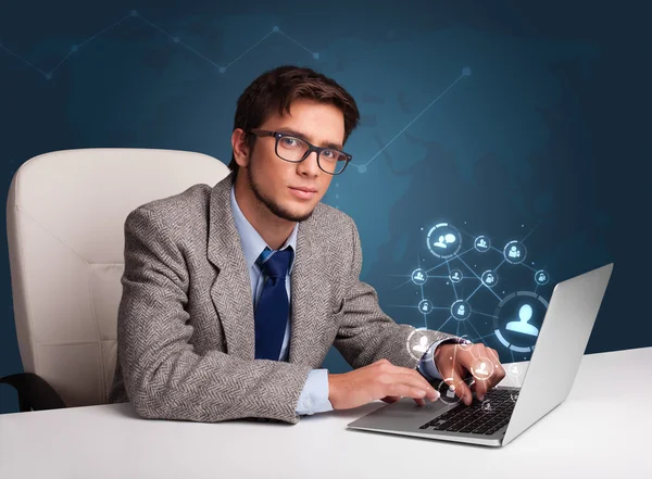 Jovem sentado na mesa e digitando no laptop com rede social — Fotografia de Stock