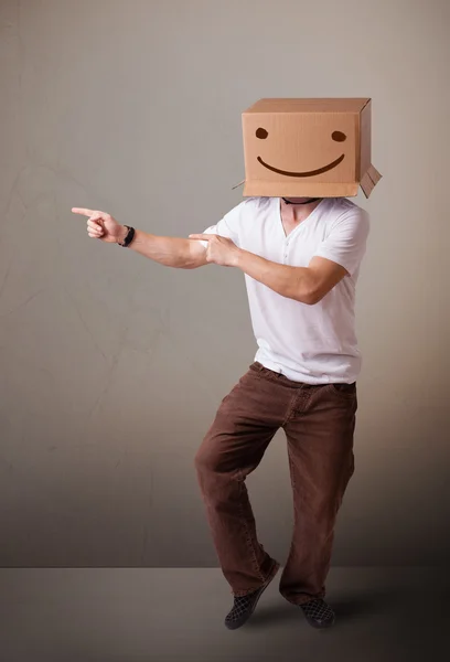 Jovem gesticulando com uma caixa de papelão na cabeça com um sorriso — Fotografia de Stock
