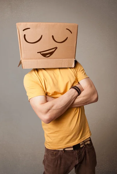 Young man gesturing with a cardboard box on his head with smiley — Stock Photo, Image