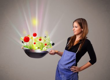 Genç bir kadın taze sebze pişiriyor.