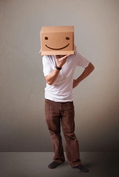 Young man gesturing with a cardboard box on his head with smiley — Stock Photo, Image