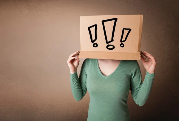 Young lady gesturing with a cardboard box on her head with excla — Stock Photo, Image