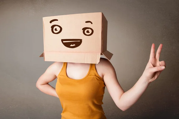 Mujer joven haciendo gestos con una caja de cartón en la cabeza con una sonrisa — Foto de Stock