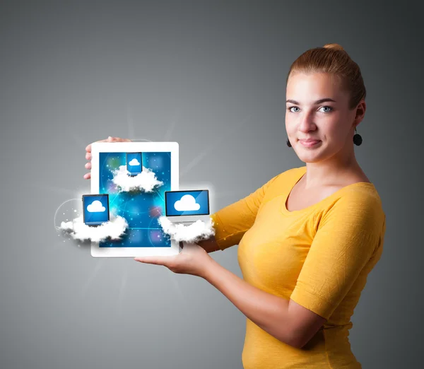 Mujer joven sosteniendo la tableta con dispositivos modernos en las nubes — Foto de Stock