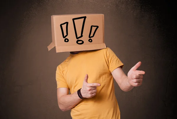 Jonge man gebaren met een kartonnen doos op zijn hoofd met exclam — Stockfoto