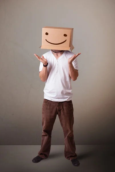 Jovem gesticulando com uma caixa de papelão na cabeça com um sorriso — Fotografia de Stock