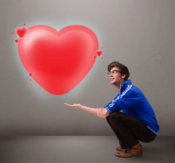 Genç adam elinde 3 boyutlu kırmızı bir kalp tutuyor. — Stok fotoğraf