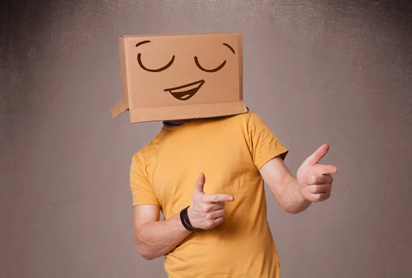 Jeune homme gesticulant avec une boîte en carton sur la tête avec un sourire — Photo