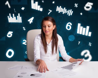 Masasında şema ve istatistiklerle oturan genç iş kadını.