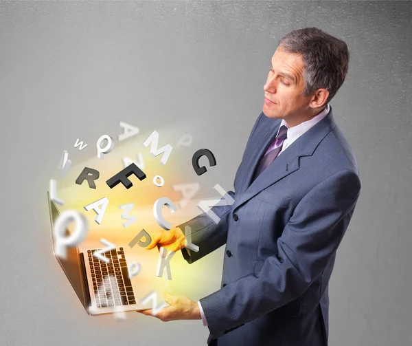 Biznesmen w średnim wieku trzyma laptopa z kolorowymi literami — Zdjęcie stockowe