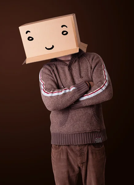 Young man gesturing with a cardboard box on his head with smiley — Stock Photo, Image