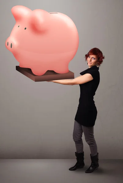 Jovem segurando uma enorme poupança porquinho banco — Fotografia de Stock
