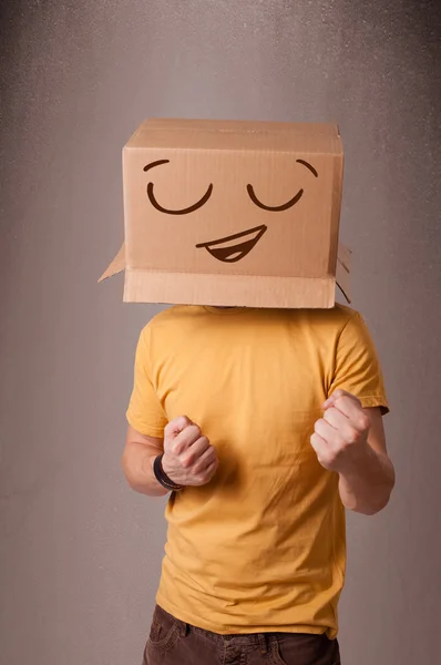 Jovem gesticulando com uma caixa de papelão na cabeça com um sorriso — Fotografia de Stock