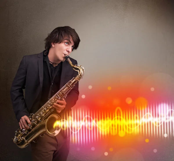 Молодой человек играет на саксофоне с красочными звуковыми волнами — стоковое фото