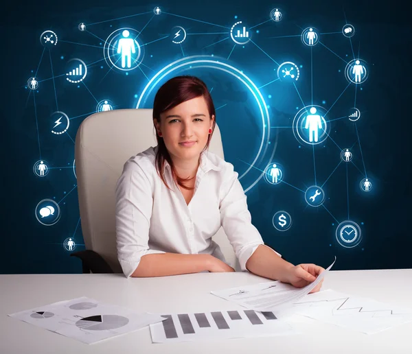 Businesswoman sitting at desk with social network icons — Stock Photo, Image