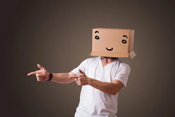 Молодой человек жестом с картонной коробкой на голове с улыбкой — стоковое фото