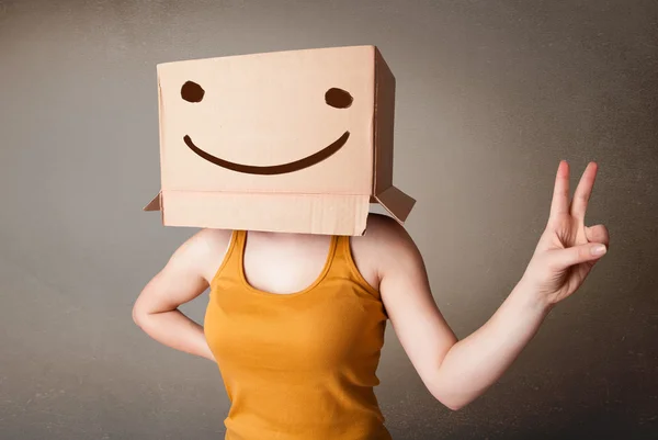 Joven haciendo un gesto con una caja de cartón en la cabeza con sonriente — Foto de Stock