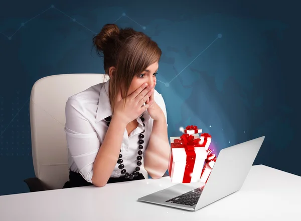 Hübsche Dame sitzt am Schreibtisch und tippt auf Laptop mit Geschenk bo — Stockfoto