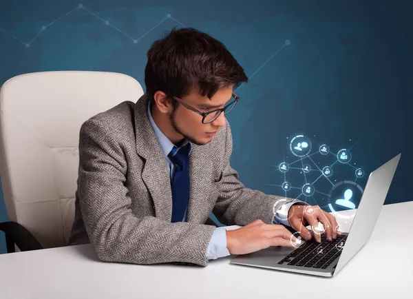 Jeune homme assis au bureau et tapant sur un ordinateur portable avec réseau social — Photo