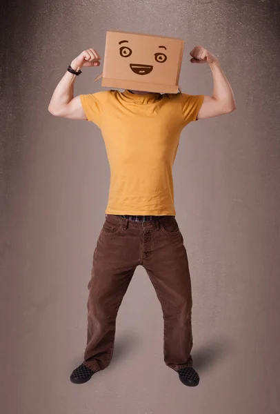 若い男の笑顔と彼の頭の上の段ボール箱で身振りで示す — ストック写真