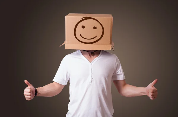 Jeune homme gesticulant avec une boîte en carton sur la tête avec un sourire — Photo