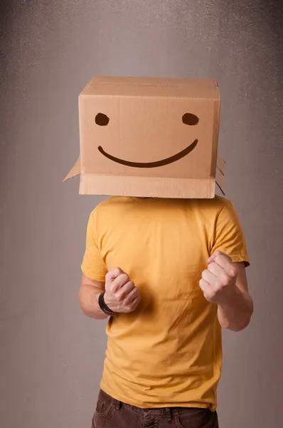 Young man gesturing with a cardboard box on his head with smiley — Stock Photo, Image