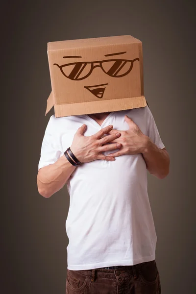 Молодий чоловік жестикулює з картонною коробкою на голові зі смайликом — стокове фото