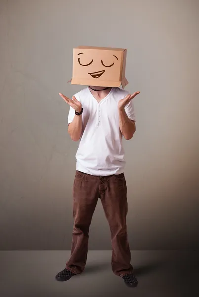 Young man gesturing with a cardboard box on his head with smiley — Stock Photo, Image