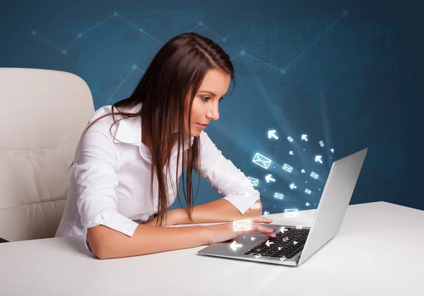 Young lady sitting at dest and typing on laptop with message ico — Stock Photo, Image