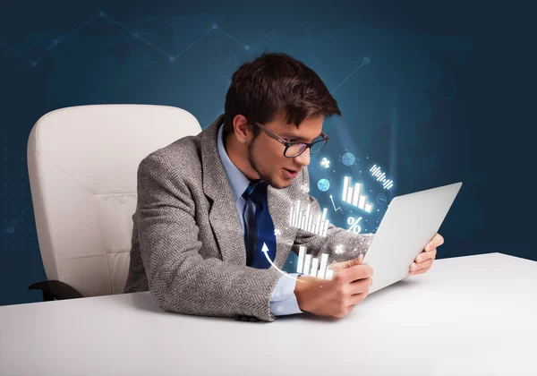 Jeune homme assis au bureau et tapant sur ordinateur portable avec des diagrammes et — Photo