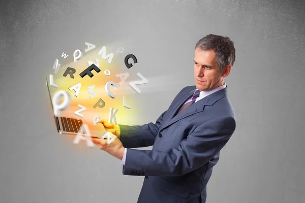 Biznesmen w średnim wieku trzyma laptopa z kolorowymi literami — Zdjęcie stockowe