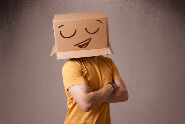 Jovem gesticulando com uma caixa de papelão na cabeça com um sorriso — Fotografia de Stock