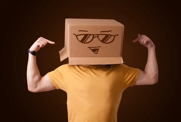 Joven haciendo un gesto con una caja de cartón en la cabeza con sonriente — Foto de Stock